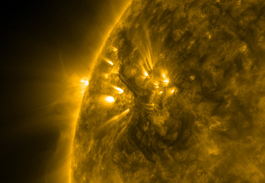 Aus einem Ausschnitt der Sonne strömen helle Lichter entlang von Magnetfeldlinien, dazwischen schwebt eine dunkle Wolke. Links ist der Sonnenrand, über dem ein heller Nebel aufsteigt.
