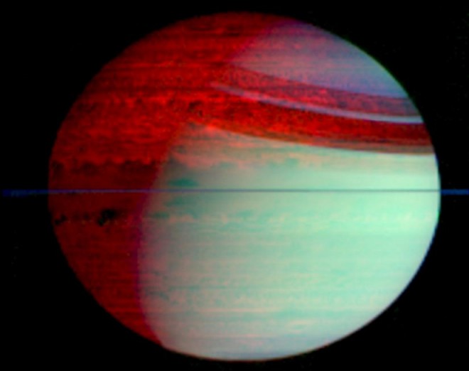Der Planet Saturn leuchtet rechts unten grün, links oben scheint er von innen heraus rot zu leuchten. Rechts oben sind die Schatten der Ringe zu sehen, die Ringe selbst sind der waagrechte dünne Strich in der Mitte.