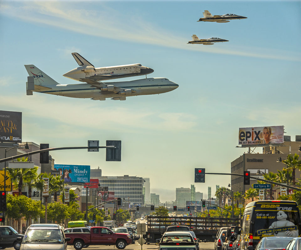 Über einer Straße von Los Angeles fliegt die Raumfähre Endeavour zum Flughafen LAX auf einer Boeing 747, davor fliegen zwei Begleitflugzeuge.