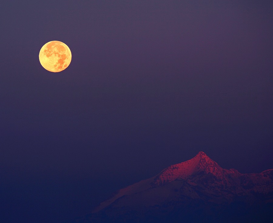 Über dem Gipfel Rocciamelone in den italienischen Alpen, der vom Sonnenaufgang rot beleuchtet wird, geht der Vollmond unter.