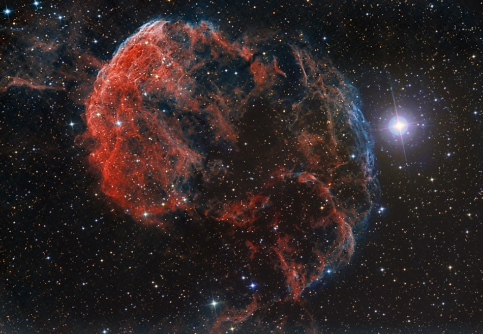 Hinter dünn verteilten Sternen leuchtet links neben dem hellen Stern Eta Geminorum im Sternbild Zwillinge ein quallenförmiger Nebel.