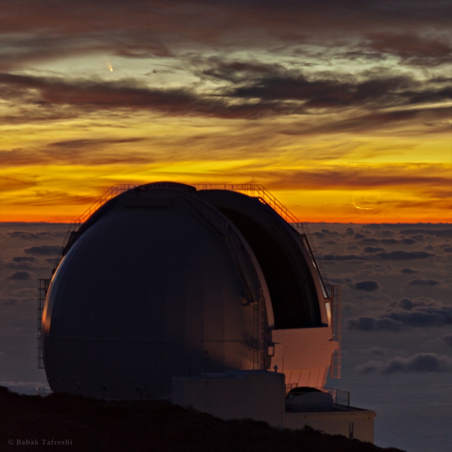 Hinter einer geöffneten Teleskopkuppel breitet sich ein Wolkenmeer aus. Darüber leuchten hinter lebhaften Wolken der Komet PanSTARRS und eine schmale Mondsichel im Abendrot.