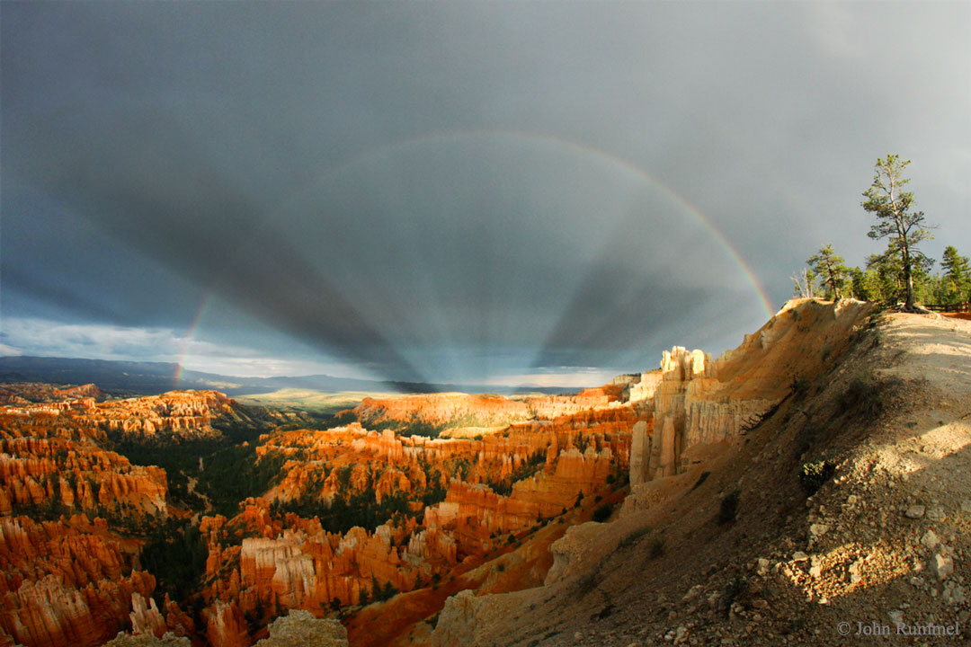 Über dem Bryce Canyon wölbt sich ein Regenbogen. Aus der Mitte strömen scheinbar Strahlenbüschel vom Sonnengegenpunkt aus.