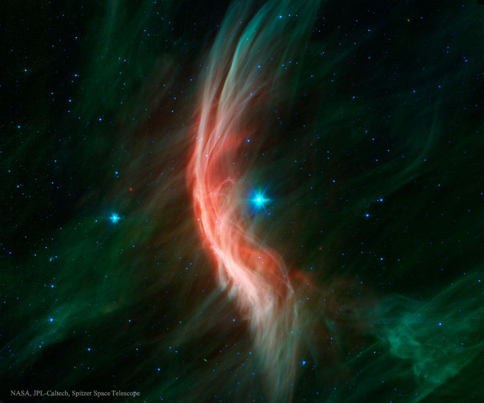 Der blaue Stern mitten im Bild treibt eine Stoßwelle vor sich her, es ist der rote Bogen, der nach links gewölbt ist. Das Bild wurde mit dem Weltraumteleskop Spitzer in Infrarotlicht aufgenommen.