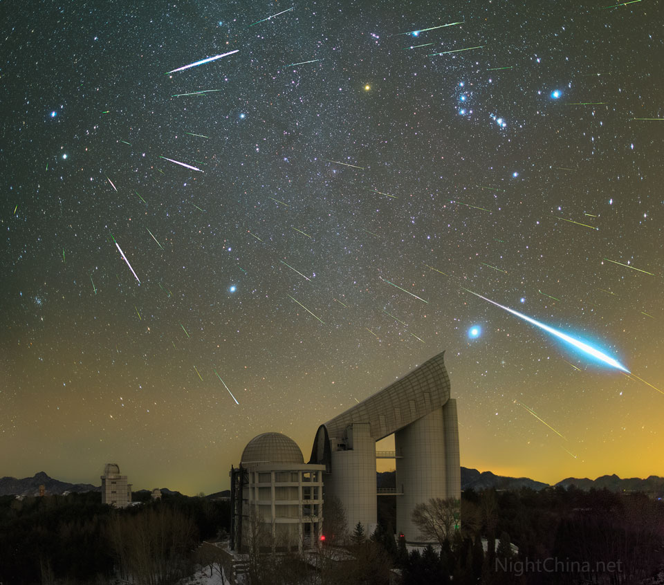 Über dem Xinglong-Observatorium ziehen Meteore der Geminiden über den Himmel. Sie strömen vom Sternbild Zwillinge aus, das links oben am Himmel steht. Rechts oben ist der Orion, darunter leuchtet eine helle Feuerkugel auf.