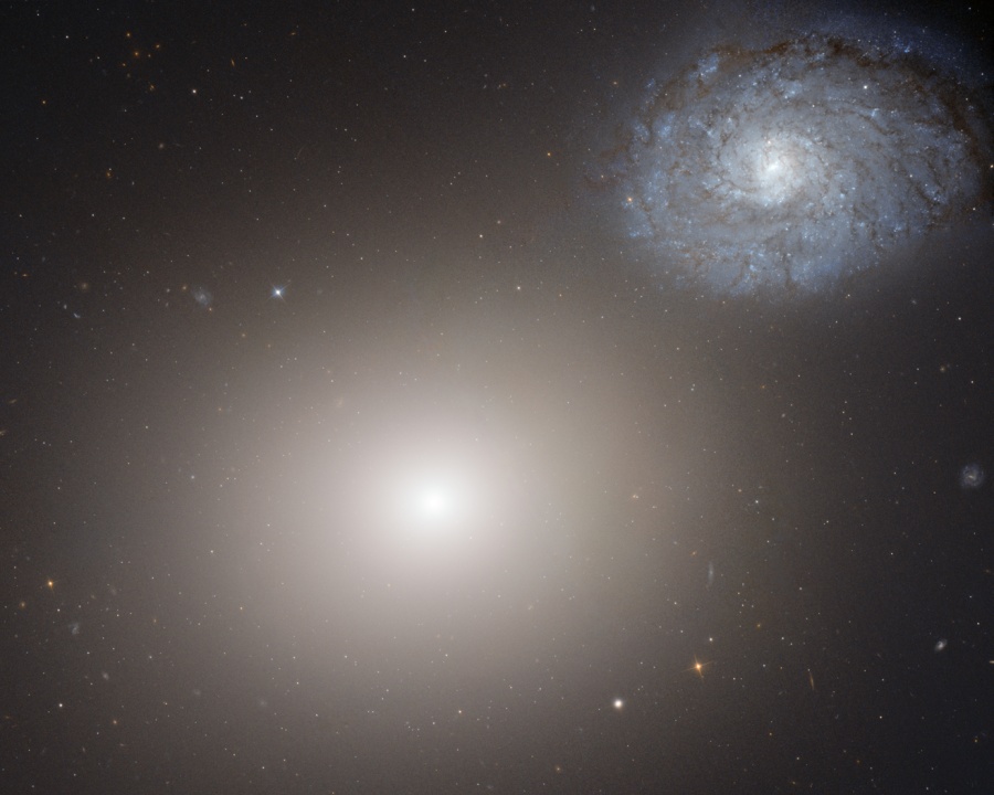 Links unten ist eine verschwommen wirkende elliptische Galaxie, rechts oben eine bläuliche Spiralgalaxie, die leicht fleckig wirkt. Die beiden sind durch Gravitation miteinander verbunden.