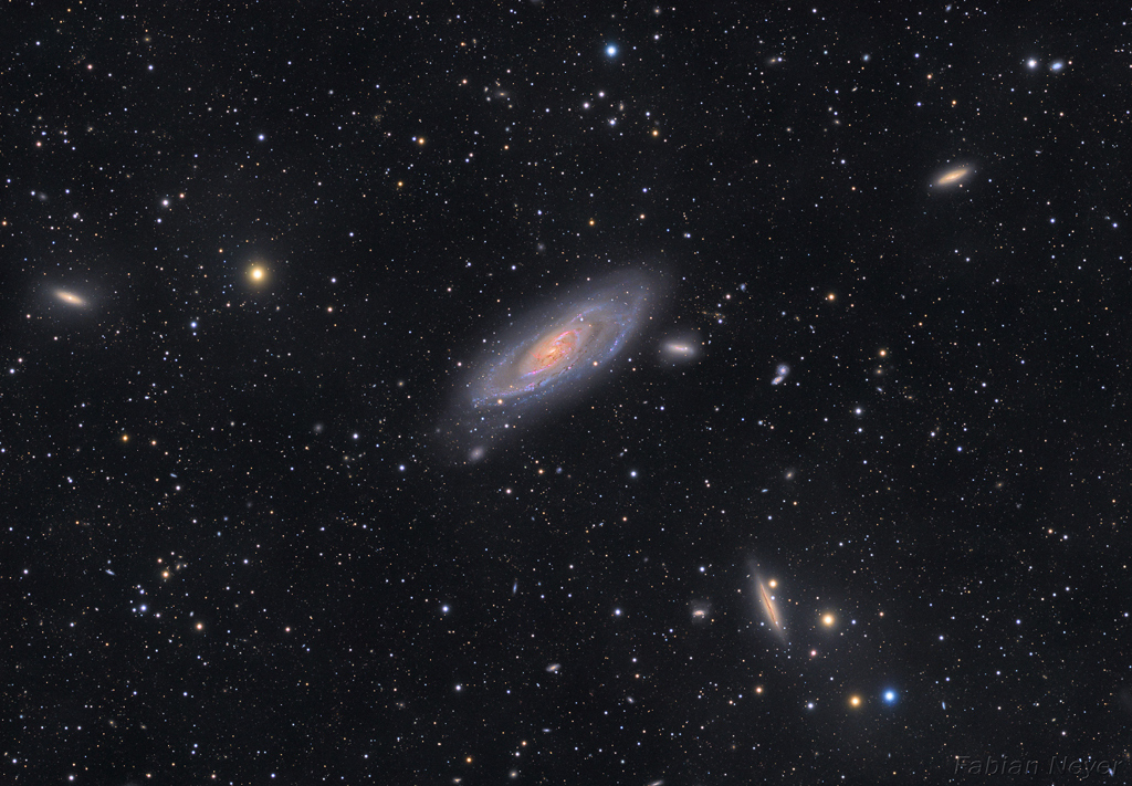Mitten im Bild leuchtet die markante Spiralgalaxie M106. Sie ist von weiteren Galaxien der Galaxiengruppe Canes-Venatici-II umgeben. Im Bildfeld sind viele Sterne verteilt.
