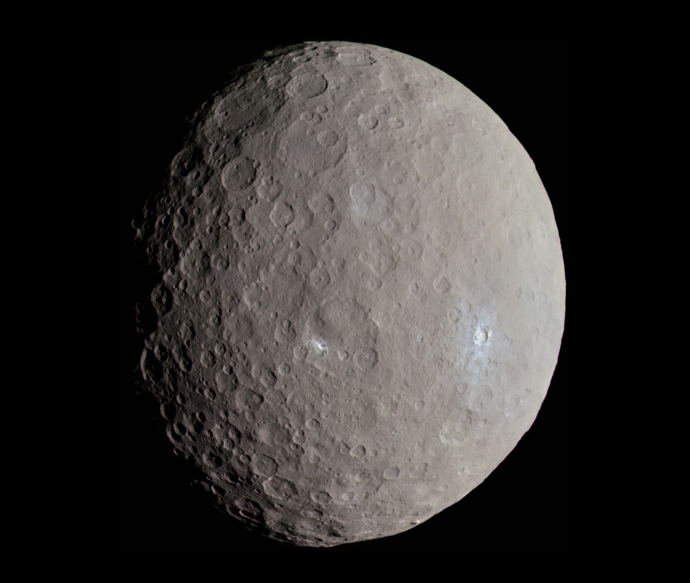 Der Zwergplanet Ceres ist flächendeckend von Kratern übersät. Links verläuft die Schattenlinie zur Nacht. In der Mitte und rechts daneben sind helle Flecken zu sehen.