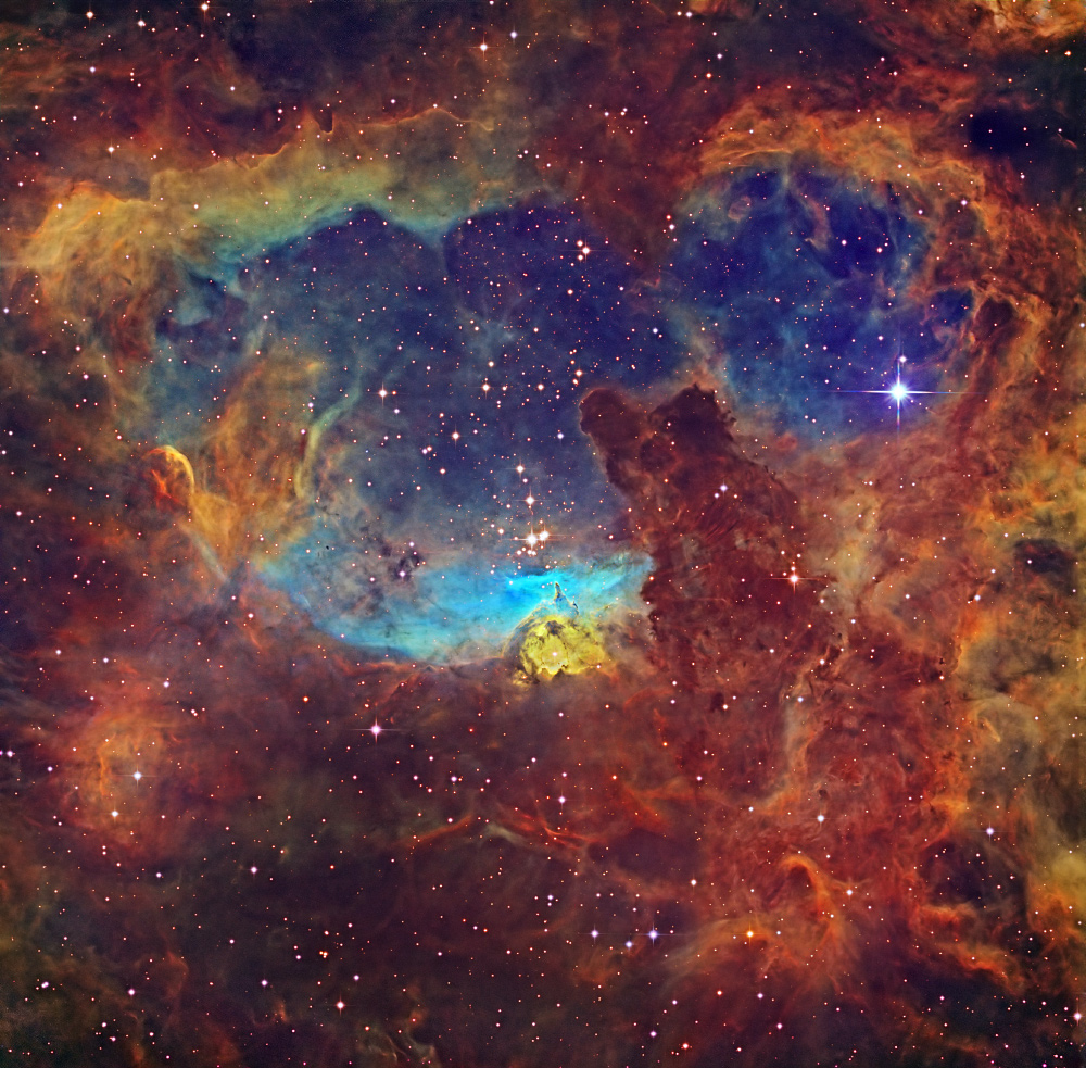 Das Panorama zeigt einen höhlenartigen Nebel. In der Mitte liegt der Sternhaufen Pismis 24. Die leuchtenden Farben wurden mit der Hubble-Farbpalette erzielt.