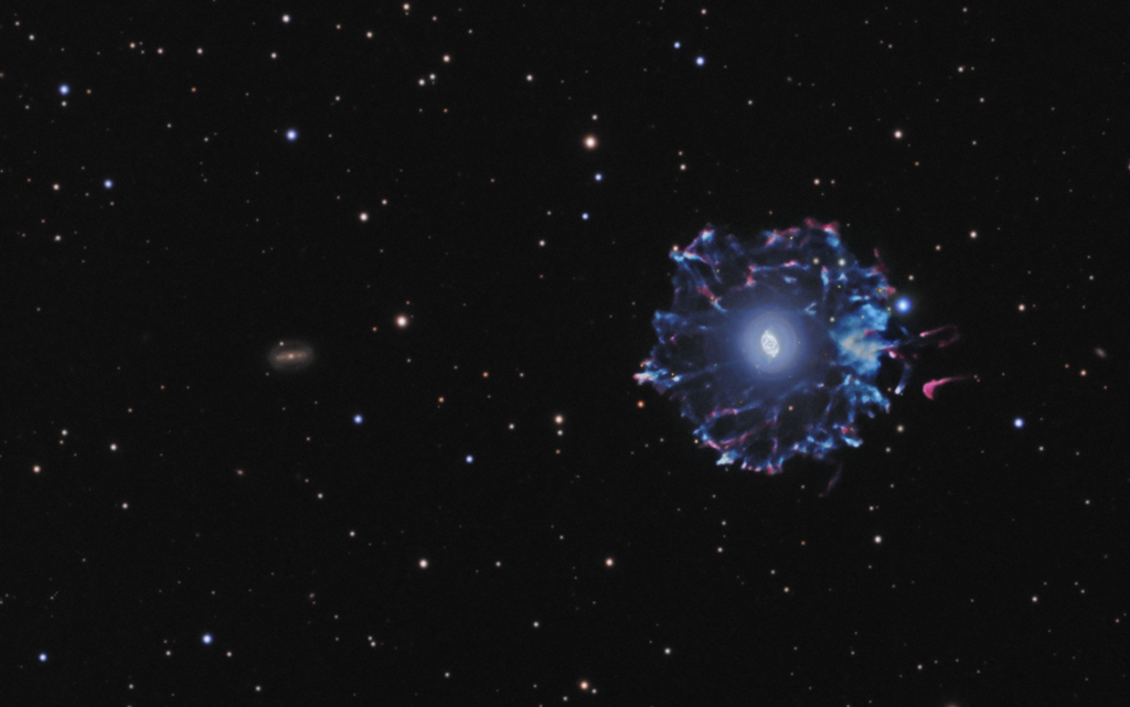 Rechts im Bild leuchtet der Katzenaugennebel NGC 6543 in blauen Farbtönen. Das bekannte Innere ist von einem wenig bekannten verschlungenen Hof umgeben. Links daneben leuchtet die weit entfernte Spiralgalaxie NGC 6552.