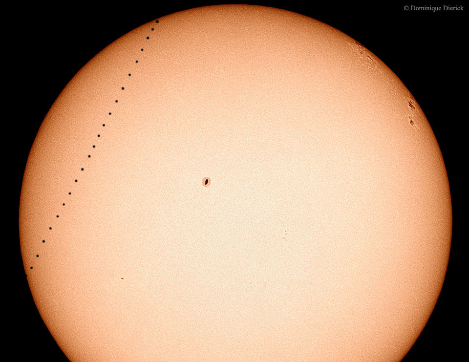 Rechts wandert der Planet Merkur beim Merkurtransit 2003 über die Sonnenscheibe. In der Mitte und rechts sind Sonnenflecken zu sehen. Der Rand der Sonne ist dunkler als die Mitte.