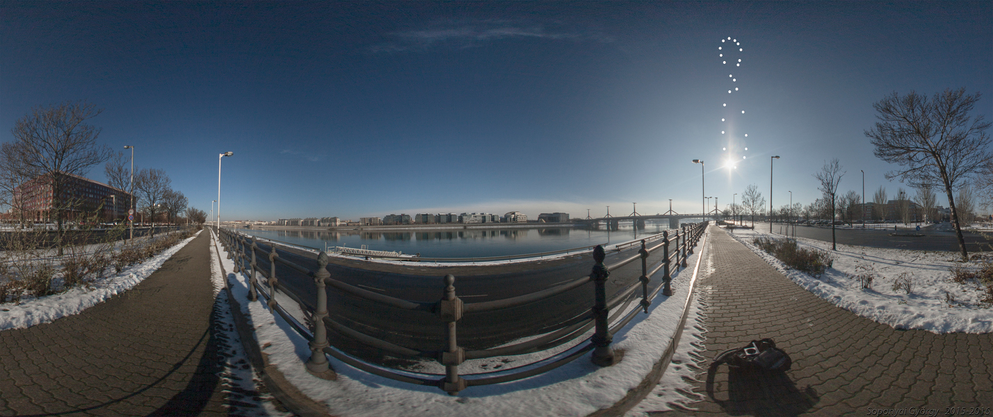 Das Fischaugenbild zeigt ein Panorama vom Ufer der Donau in Budapest. Rechts zieht die Sonne eine Schleife in Form einer 8, ein Analemma. Das Basisbild entstand im Winter, als die Sonne sehr tief stand.