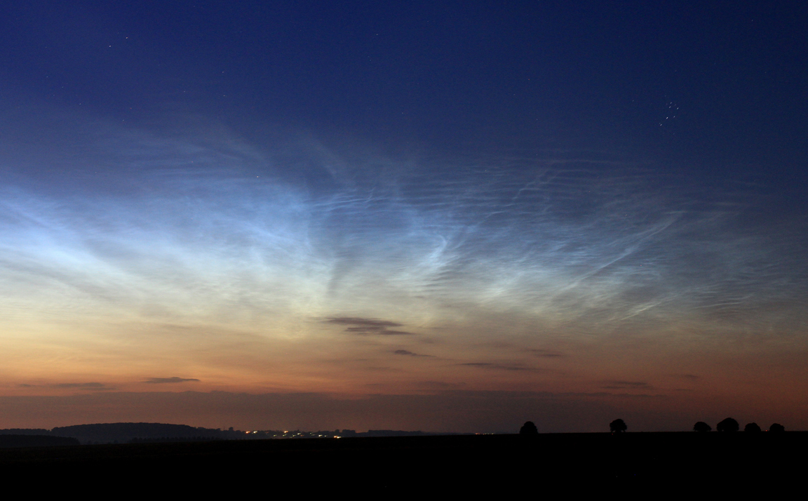 Der Himmel verläuft von Orangerot bis zu Nachtblau. Dazwischen ist ein feines Geäst weißer leuchtender Nachtwolken über dem Horizont.