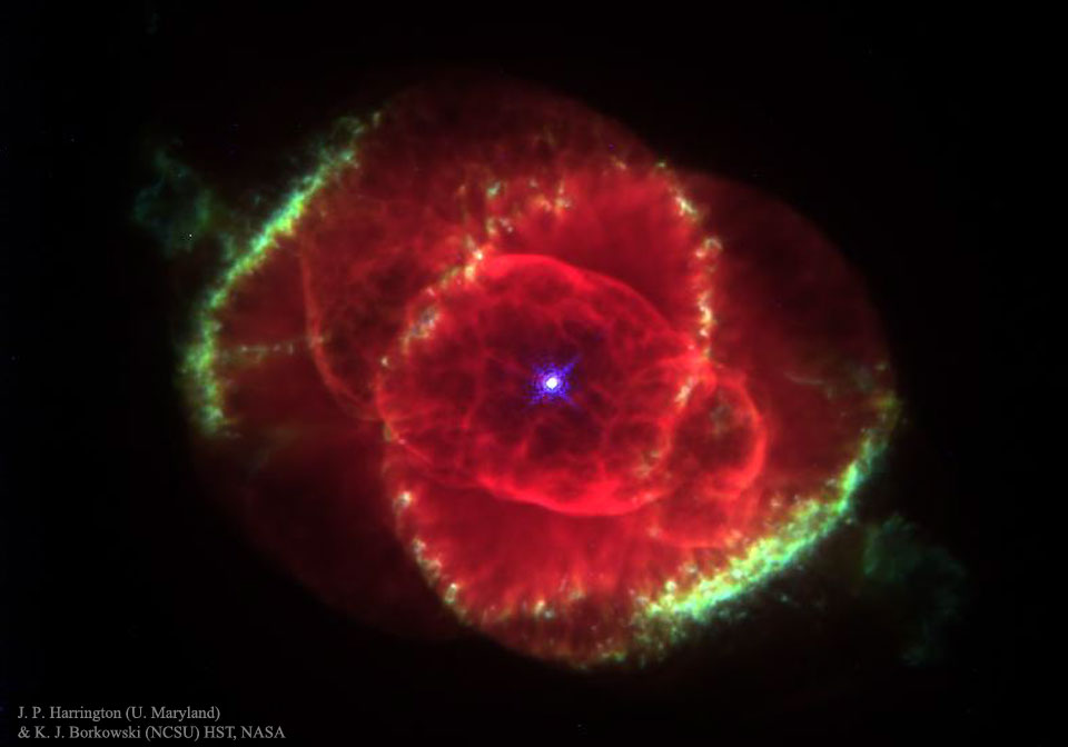 Mitten im Bild leuchtet ein roter Nebel mit verschachtelten Schalen. Links oben und rechts unten sind grün leuchtende Ränder. In der Mitte leuchtet ein blauer Stern.