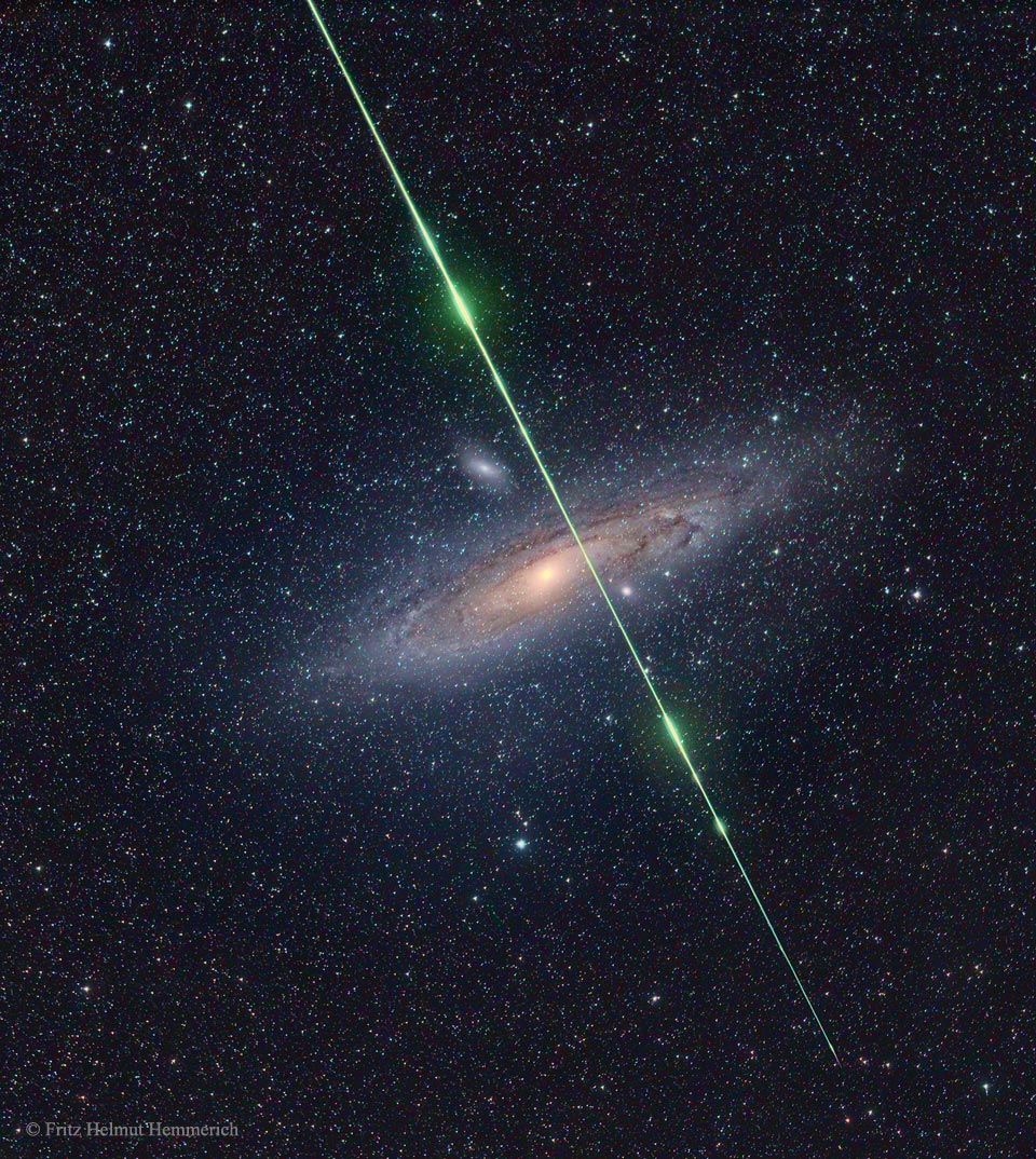 Vor der Andromedagalaxie M31 zischt ein grün lodernder Meteor vorbei.