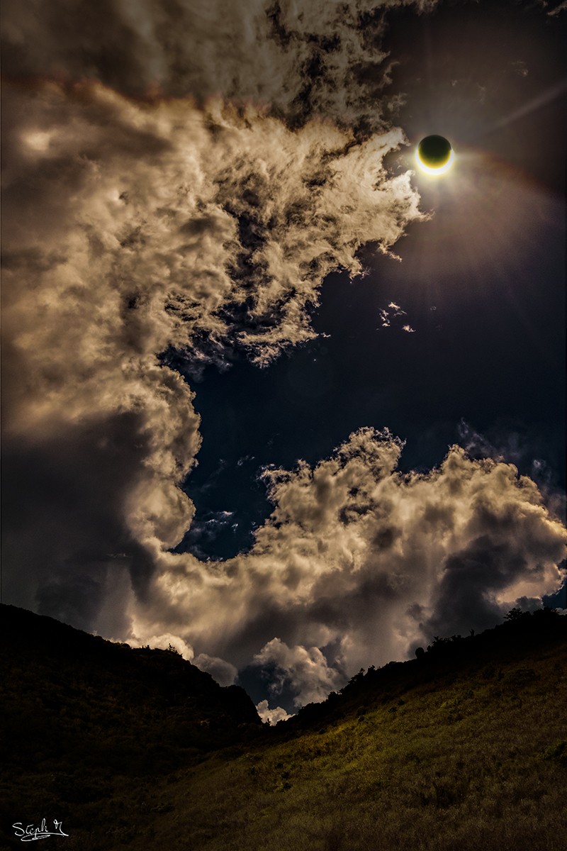 Neben dramatisch wirkenden Wolken leuchtet rechts oben die Sichel der Sonne, die fast vom Mond verdeckt ist.