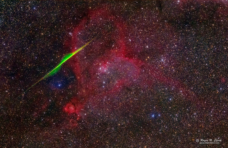 Zwischen dichten Sternwolken zeichnet sich eine tiefrot leuchtende Nebelstruktur ab, die an ein Herz erinnert. Sie wird im von einem Pfeil getroffen. Der Pfeil ist ein grün leuchtender Meteor.