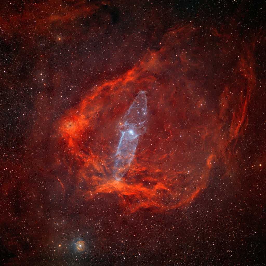 Mitten im Bild schimmert eine fragile längliche weiß-bläuliche Form. Es ist der Nebel Ou4. Er ist von einer rot leuchtenden Gashülle umschlossen. Möglicherweise ist Ou4 ein Ausfluss des Sterns HR8119.