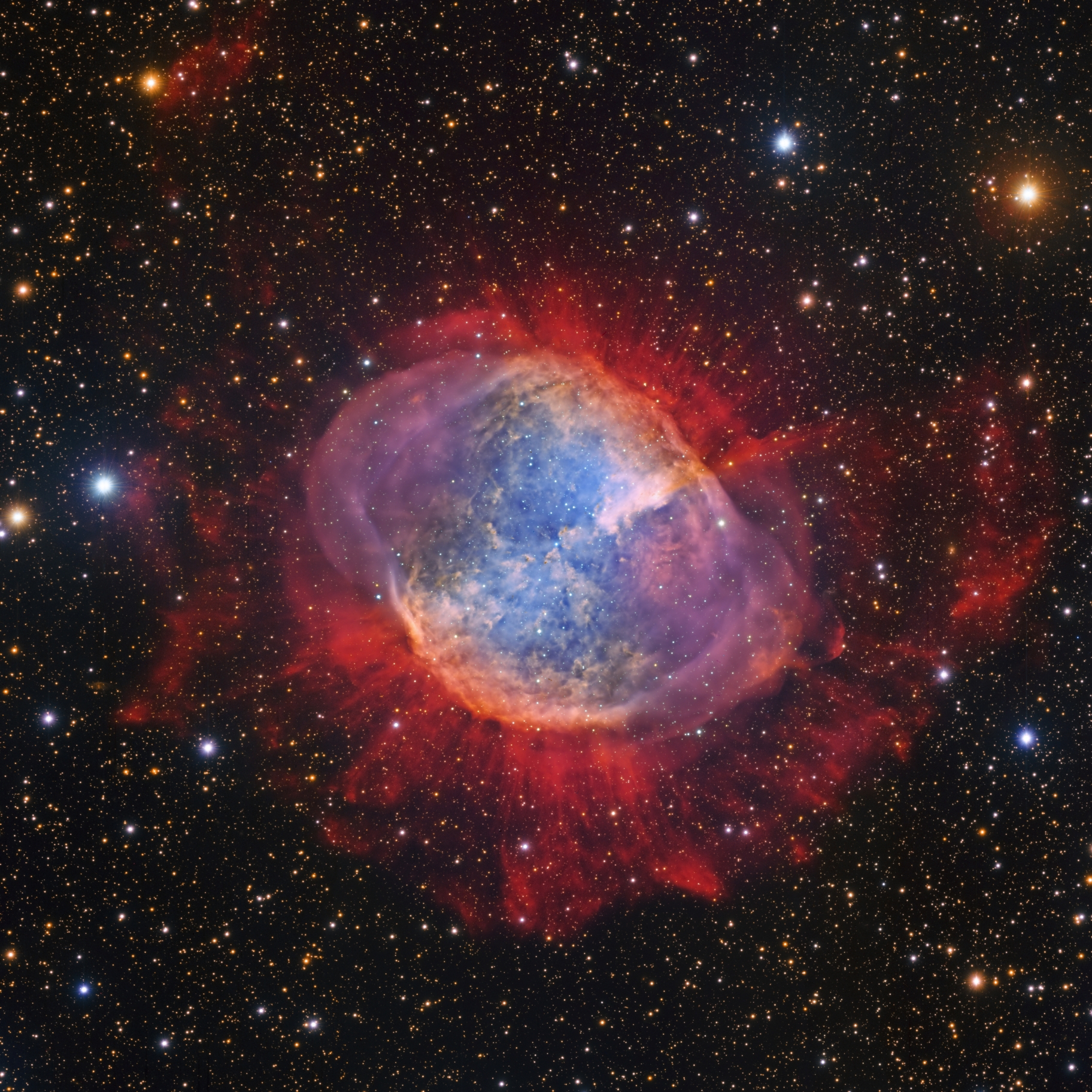Mitten im Bild leuchtet ein bläulicher, wolkiger runder Nebel, der von roten Wolken umgeben ist. Im Hintergrund sind Sterne verteilt.