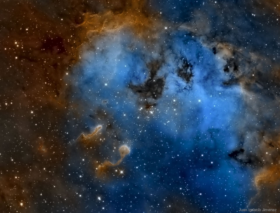 In einem blau schimmernden Teich, der von braunen und dunklen Staubwolken umgeben ist, schwimmen unten zwei Gebilde, die an Kaulquappen erinnern.