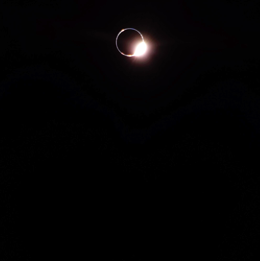 Vor einem schwarzen Hintergrund steht oben im Bild ein kleiner heller, leicht unscharfer Ring. Rechts unten leuchtet am Ring ein heller Fleck wie ein Diamant.