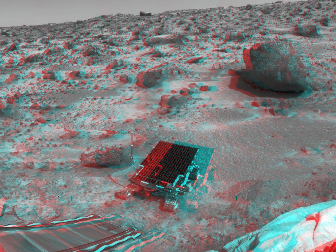 Die Anaglyphe zeigt die Marsoberfläche mit dem Mars Pathfinder, dem Rover Sojourner, einer Rampe und Felsen. Mit rot-blauen Brillen wirkt das Bild dreidimensional.